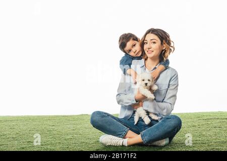 Lächelnde Mutter, die Havanese Welpe und Sohn hält, die sie isoliert auf Weiß umarmen Stockfoto