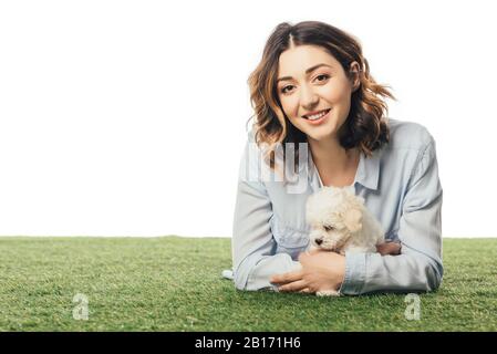 Lächelnde Frau, die Havanese Welpe hält und auf Gras liegt, isoliert auf Weiß Stockfoto