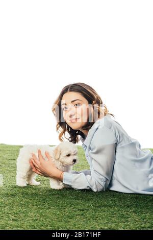 Lächelnde Frau, die Havanese Welpe hält und auf Gras liegt, isoliert auf Weiß Stockfoto