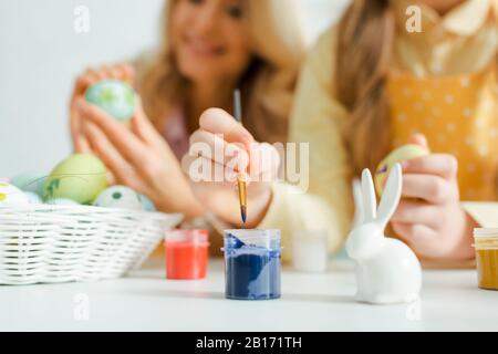 Selektiver Fokus der dekorativen Brötchen in der Nähe von Kindern, die Pinsel in der Nähe des Mixbechers mit Farbe halten Stockfoto