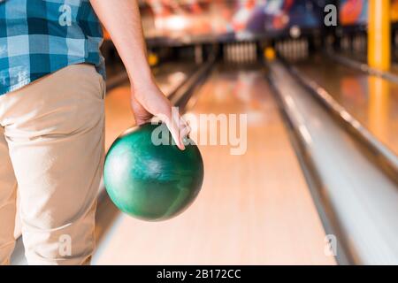 Teilansicht des jungen Mannes, der Bowlingball in der Nähe der Kegelbahn hält Stockfoto
