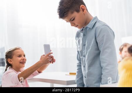Selektive Fokussierung des grausamen Kindes lächelnd, während Foto von Mobbing Klassenkameraden, Cyberbullying Konzept Stockfoto
