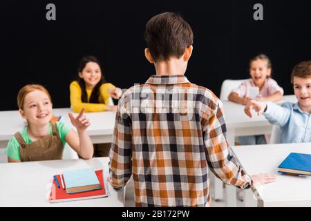 Rückansicht des Schuljungen, der in der Nähe von Schulkindern steht und mit den Fingern auf schwarzem, Mobbingkonzept zeigt Stockfoto