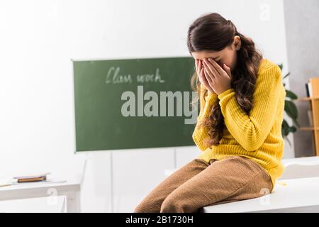 Verärgert und drangsaliert Schulmädchen, die im Klassenzimmer weinend das Gesicht bedecken Stockfoto