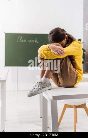 Traurige und drangsalierte Schulmädchen, die im Klassenzimmer weinend das Gesicht bedecken Stockfoto