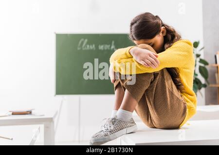 Schikanierte Schulmädchen, die Gesicht bedecken, während sie im Klassenzimmer weinten Stockfoto