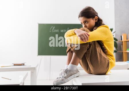Verärgert und drangsaliert Schulmädchen, die allein im Klassenzimmer sitzen Stockfoto