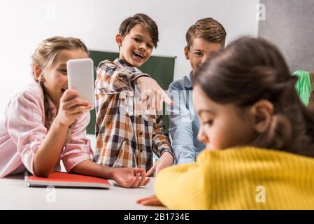 Selektiver Fokus der Schüler mit Smartphone und grausamen Klassenkameraden, die in der Nähe von Schikanen lachen, Cyberbullying Konzept Stockfoto