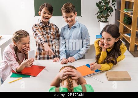 Selektiver Fokus der Schüler mit Smartphone und grausamen Klassenkameraden, die in der Nähe von Schikanen lachen, Cyberbullying Konzept Stockfoto