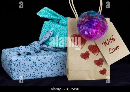In Stoff verpacktes Geschenk und selbstgemachter Pompom auf schwarzem Hintergrund. Machen, recyceln und wiederverwenden für nachhaltige Vergaben für Feiertage und Geburtstage, ohne Verschwendung Stockfoto