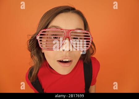 Überrascht kleines Mädchen Schuluniform. Party Brille für Spaß. Kid Mode Konzept. Aufenthalt mit Brille konzentriert. cool aussehende Schüler orange hinterlegt. hübsche und stilvolle Kind. Party Elemente. Stockfoto