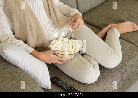 Zugeschnittene Frau auf dem Sofa, die Popcorn isst Stockfoto