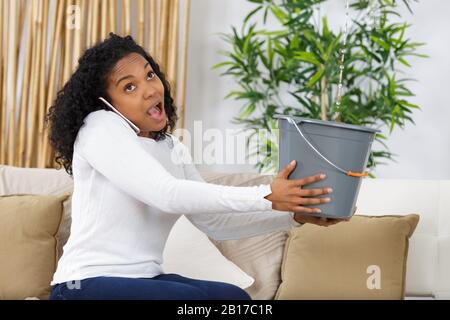 Überraschte Frau am Telefon, die undichte Deckenwasser sammelt Stockfoto