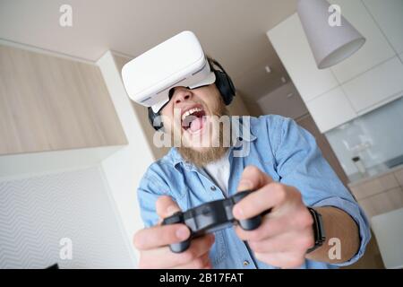 Aufgeregter junger Mann mit vr-Brille, die den Controller beim Spielen von Videospielen hält Stockfoto