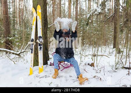 Frau mit Skiern auf Schlitten im Winterwald, die Schnee in die Luft wirft Stockfoto