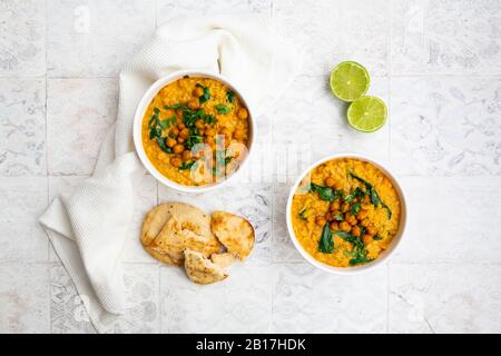 Veganes Linsencurry mit roten Linsen, Süßkartoffeln, Spinat, gerösteter Kurkuma, Kichererbsen, mit Limettensaft und Koriander und Naanbrot Stockfoto