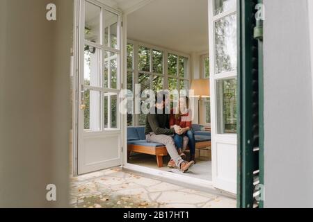Glückliches Paar sitzt im Wintergarten, spricht und hält die Hände Stockfoto