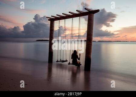 Frau auf einem Schaukel am Meer bei Sonnenuntergang, Maguhdhuvaa-Insel, Gaafu Dhaalu Atoll, Malediven Stockfoto