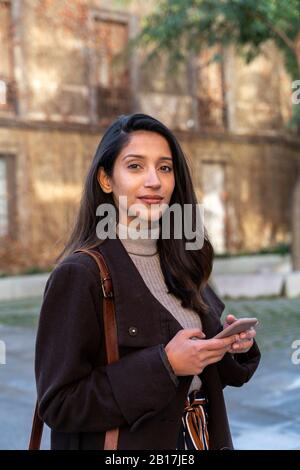 Porträt der selbstbewussten jungen Frau mit Smartphone in der Stadt Stockfoto
