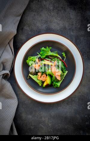 Teller mit grünem Salat mit Maissalat, Rucola, Spinat, rotem Blattsalat, Rote-Bete-Blätter, Avocado, Lachsfleisch und Balsamico-Essig Stockfoto