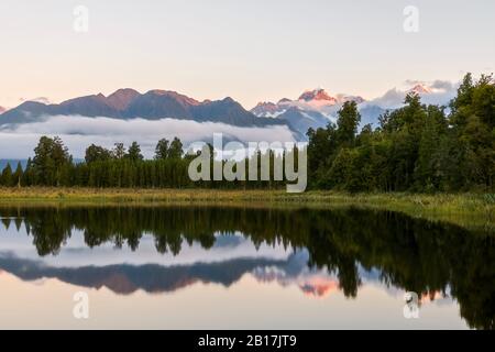 Neuseeland, Westland District, Fox Glacier, Lake Matheson spiegeln umliegenden Wald und entfernten Bergkette Stockfoto