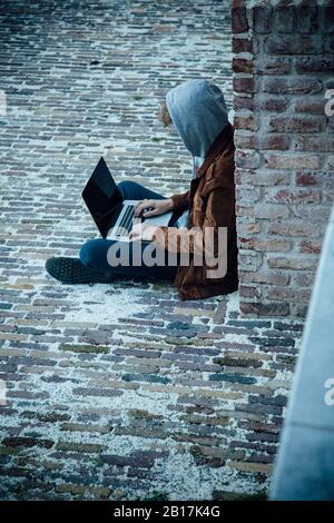 Teenager mit Laptop und sitzen auf einem Steinboden in der Stadt Stockfoto