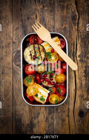 Lunchbox mit Tomatensalat mit gegrilltem Gemüse und Halloumi-Käse, Granatapfelkernen, Sumac, schwarzem Sesam und Petersilie Stockfoto