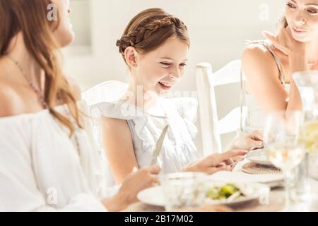 Fröhliches Mädchen und zwei Frauen beim gemeinsamen Mittagessen Stockfoto