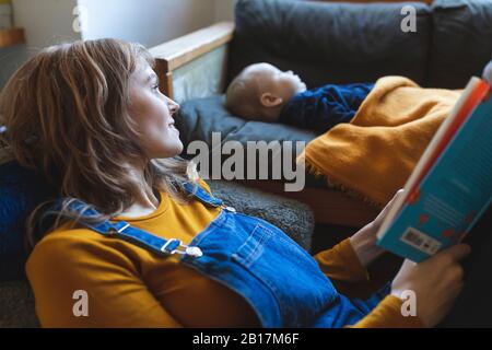 Frau liest Buch im Wohnzimmer mit kleinem Sohn schlafend Stockfoto