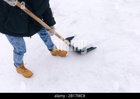 Schnittansicht der Frau, die den Gehweg mit einer Schneeschaufel freiräumt Stockfoto