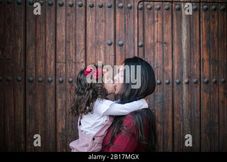 Mutter hält und küsst kleine Tochter draußen Stockfoto