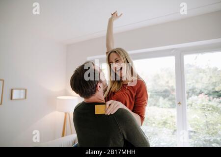Glückliches Paar, das zu Hause steht und seine Kreditkarte hält Stockfoto