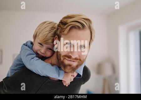 Portrait eines lächelnden Vaters, der den Sohn zuhause zurückträgt Stockfoto