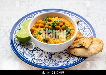 Veganes Linsencurry mit roten Linsen, Süßkartoffeln, Spinat, gerösteter Kurkuma, Kichererbsen, mit Limettensaft und Koriander und Naanbrot Stockfoto