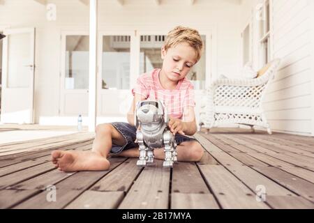 Junge spielt mit Roboter Hund auf der Veranda Stockfoto