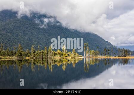 Neuseeland, Grauen Bezirk, Inchbonnie, bewaldeter Hügel, der sich im Brunner See spiegelt Stockfoto