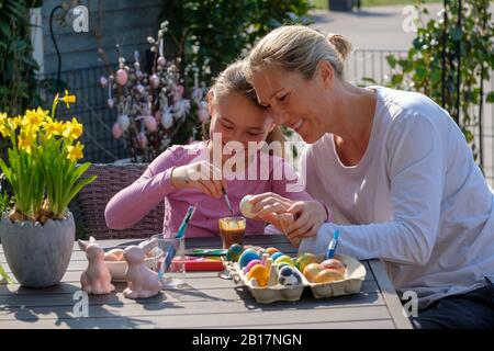 Glückliche Mutter und Tochter, die am Gartentisch sitzen und Ostereier malen Stockfoto