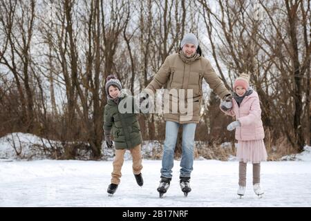 Zwei glückliche Geschwister, die gemeinsam mit dem Vater auf Eis laufen Stockfoto