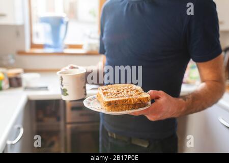 Nahaufnahme des Menschen in der Küche mit Sandwiches und einem Becher Stockfoto