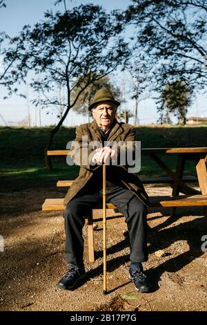 Alter Mann mit Stock auf Banch in einem Park sitzen Stockfoto