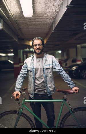 Junger Mann steht im Parkhaus mit seinem Fixie-Fahrrad Stockfoto