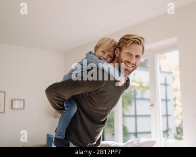 Porträt eines glücklichen Vaters, der den Sohn zuhause mit einem Huckepack trägt Stockfoto
