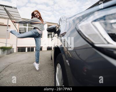 Fröhliche rotköpfige Frau springt neben dem Auto Stockfoto