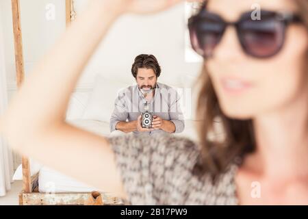 Bärtiger Mann auf dem Bett mit altmodischer Kamera mit Frau im Vordergrund Stockfoto