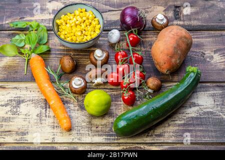 Zutaten für Süßkartoffel-Curry (Süßkartoffel, Zucchini, Pilze, Mais, Tomaten, Zwiebeln, Knoblauch, Limette, Basilikum) Stockfoto