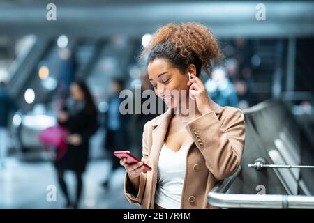 Lächelnde junge Frau mit Handy und Ohrstöpsel an der U-Bahn-Station Stockfoto