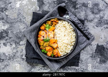 Curry mit Süßkartoffeln, Karotten, Pilzen, Zucchini, Zuckererbsen, Tomaten, Petersilie und Reis in der Schüssel Stockfoto