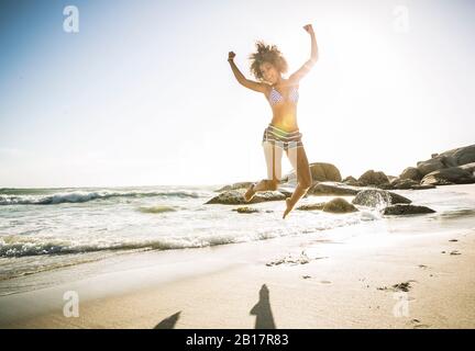Glückliche junge Frau am Strand springen Stockfoto