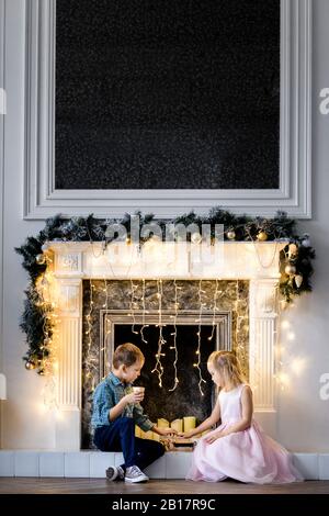 Junge und seine kleine Schwester sitzen zu Weihnachten zusammen vor dem Kamin Stockfoto
