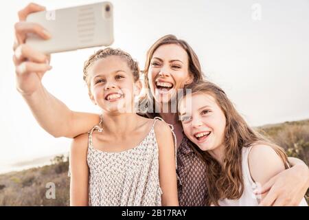 Glückliche Mutter, die ein Selfie mit ihren beiden Töchtern bei Sonnenuntergang macht Stockfoto